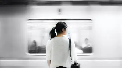 Uma mulher está olhando para a esquerda, de frente para um trem que está passando.