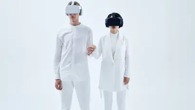 Um casal usando óculos de realidade virtual, vestido de branco e de mãos dadas.