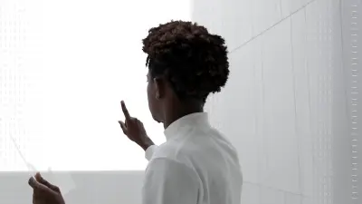 A man stands with his back to the viewer, interacting with a futuristic technology interface in a minimalist space.