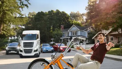 Homem em uma bicicleta com automóveis e um caminhão ao fundo